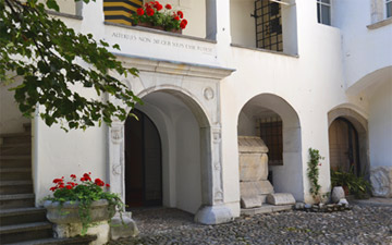 Renaissance-Arkadenhof des Stadtmuseums. Weißes Tor in den Innenhof. Links neben dem Tor steht ein Blumentrog mit roten Blumen.