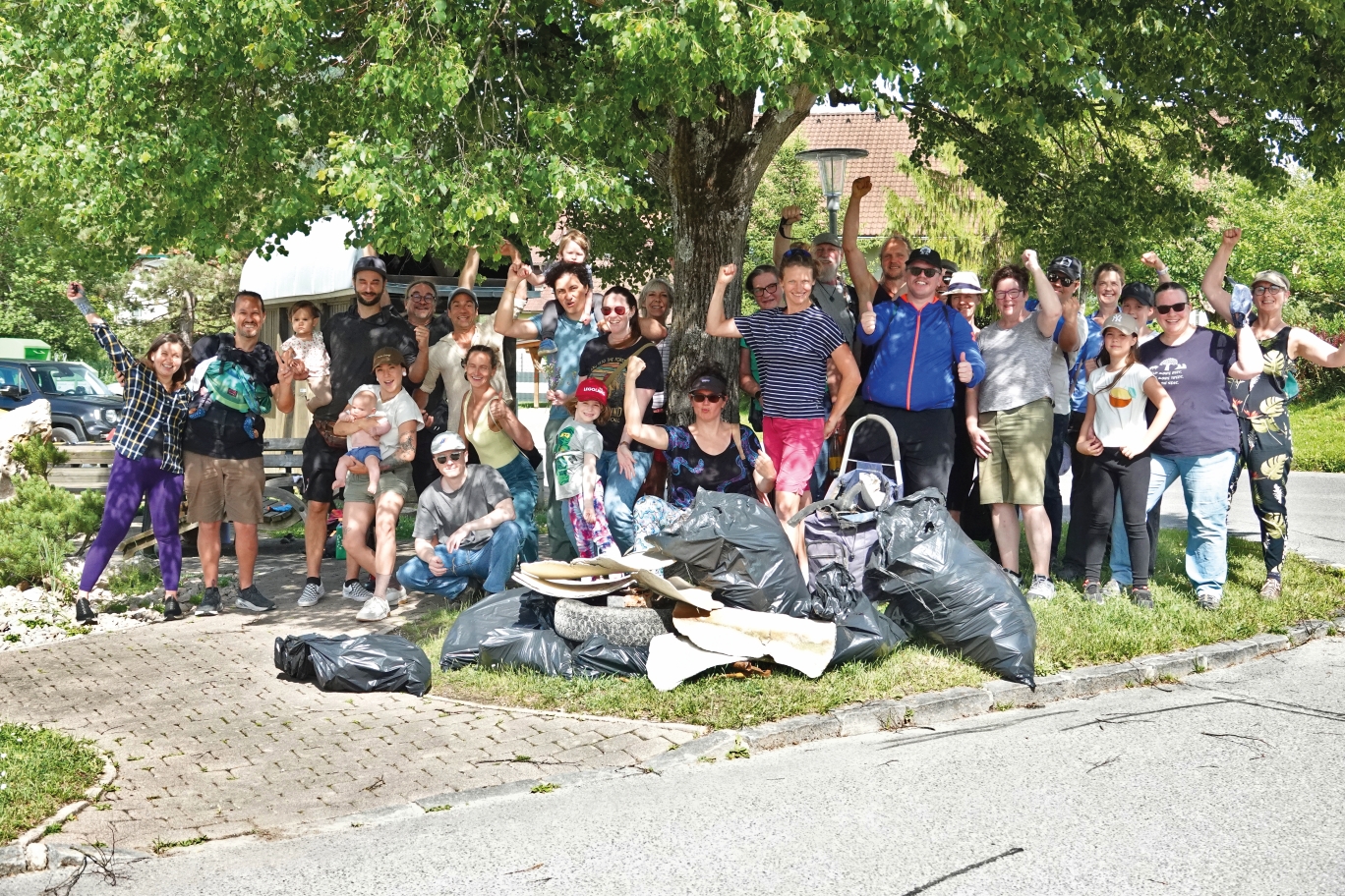 Gemeinschaft sammelt Müll in Niederösterreich, viele Menschen mit Kindern und Müllsäcken stehen vor Bäumen.
