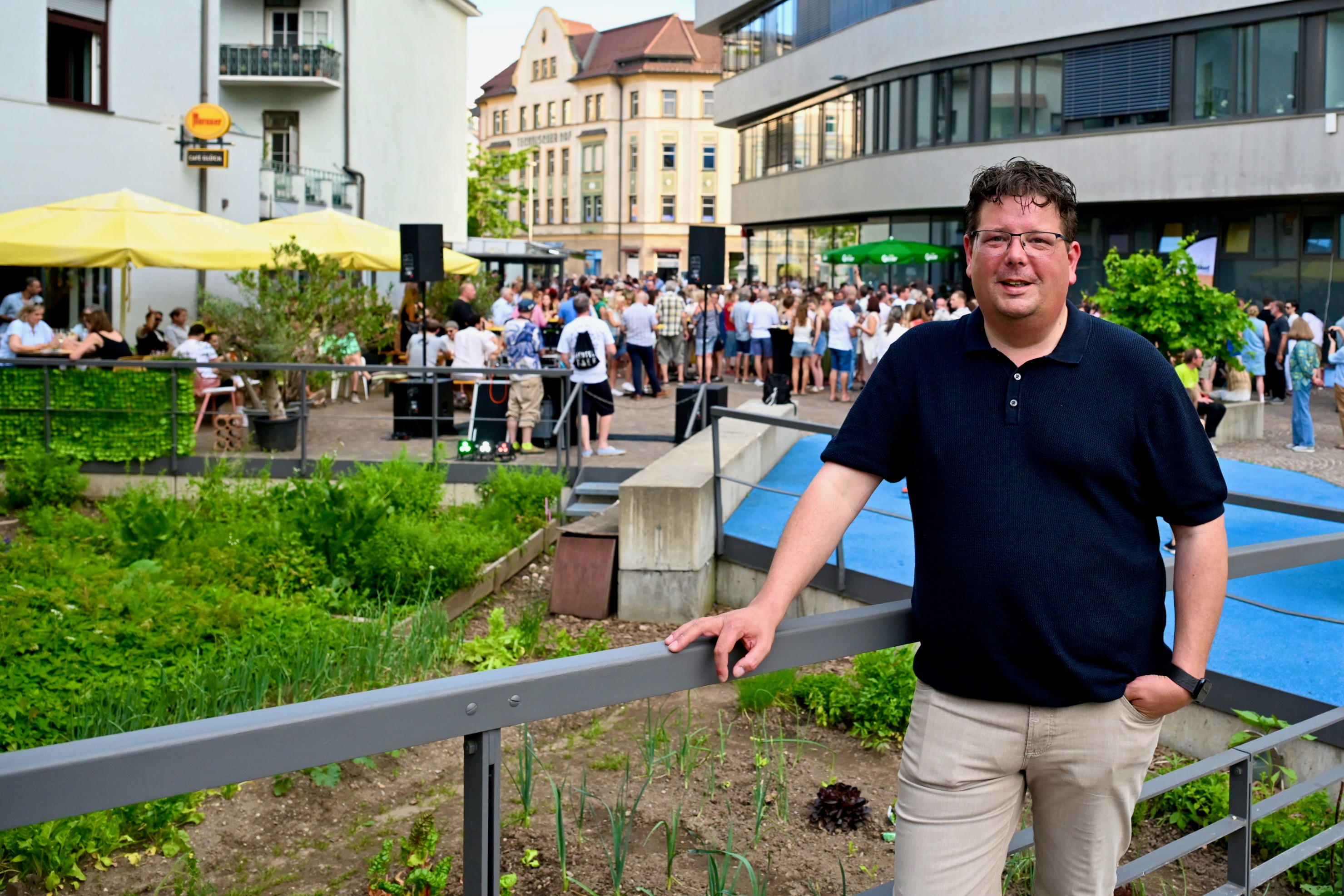 Mann mit Brille lächelt in die Kamera, im Hintergrund Menschen auf einem Fest in Österreich.