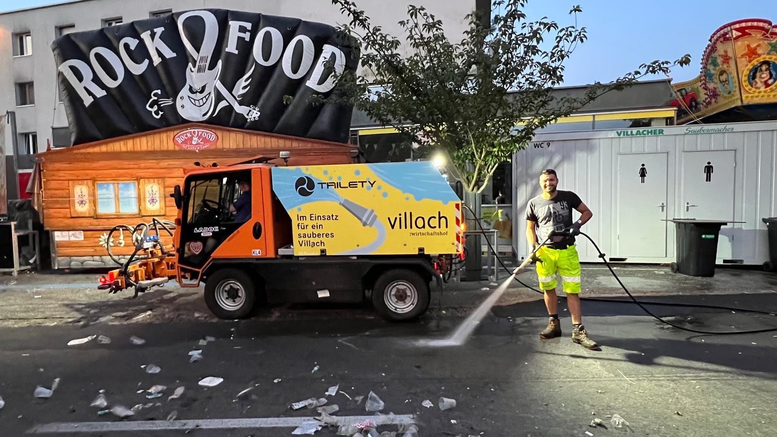 Reinigungskraft auf einem Fest in Villach mit einem Reinigungsfahrzeug und Wasserschlauch.