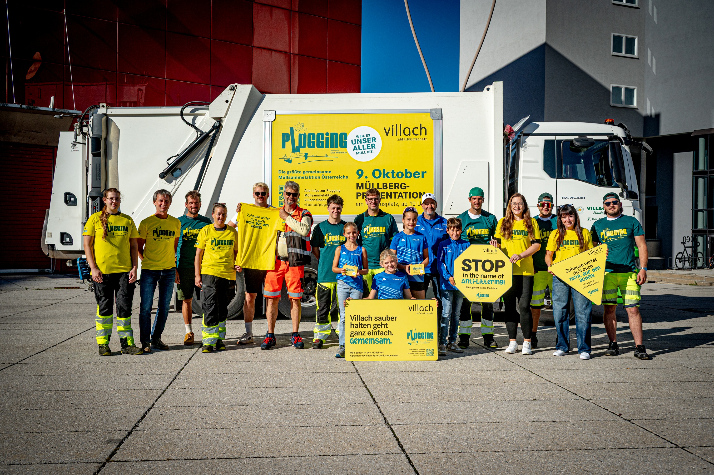 Plogging-Teilnehmer in Villach vor Müllwagen mit gelben T-Shirts und Plakaten