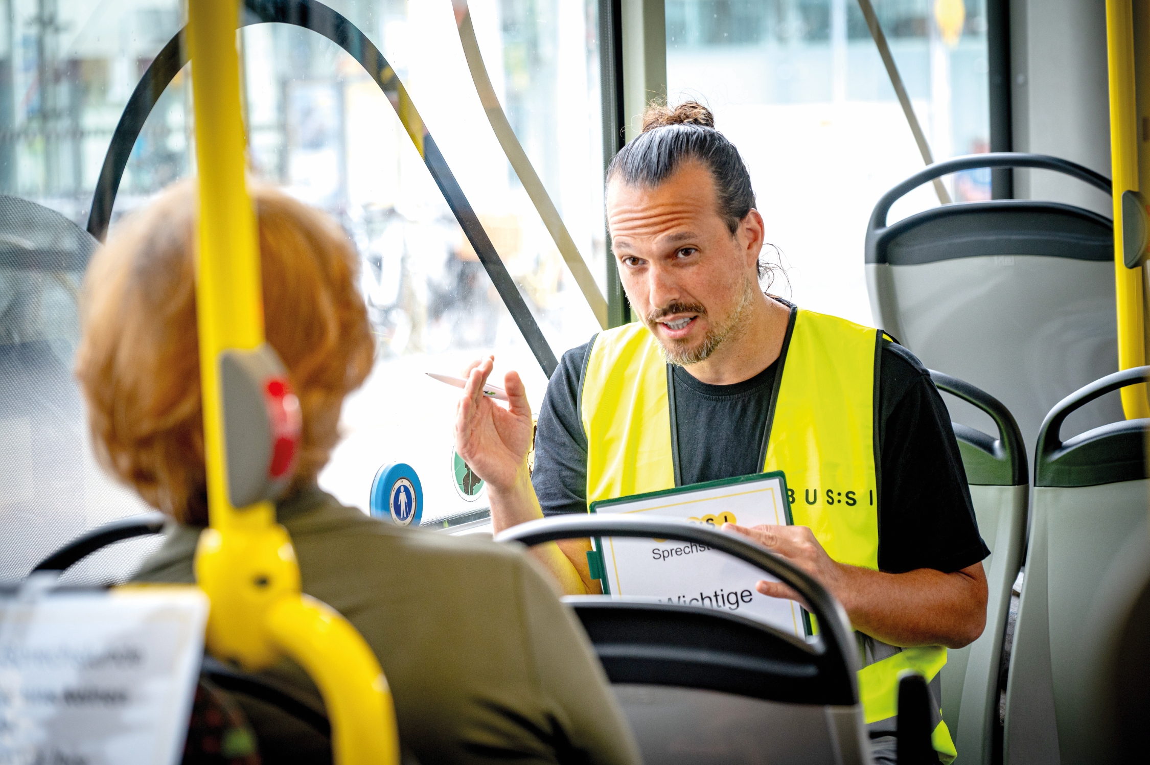 Kontrolleur mit Warnweste im Gespräch mit Fahrgast in einem Bus in Wien