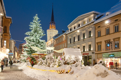 Villacher Hauptplatz im Winter bei Nacht. Im Hintergrund leuchtet der Stadtkirchtum in seiner Weihnachtsbeleuchtung