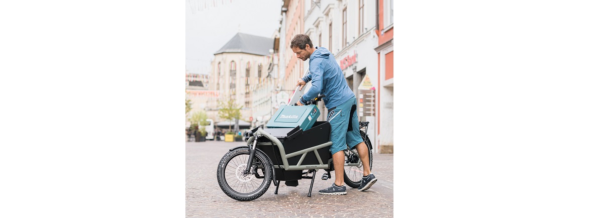 ein sportlich gekleideter Mann legt ein Brett in den Behälter von einem Lastenfahrrad