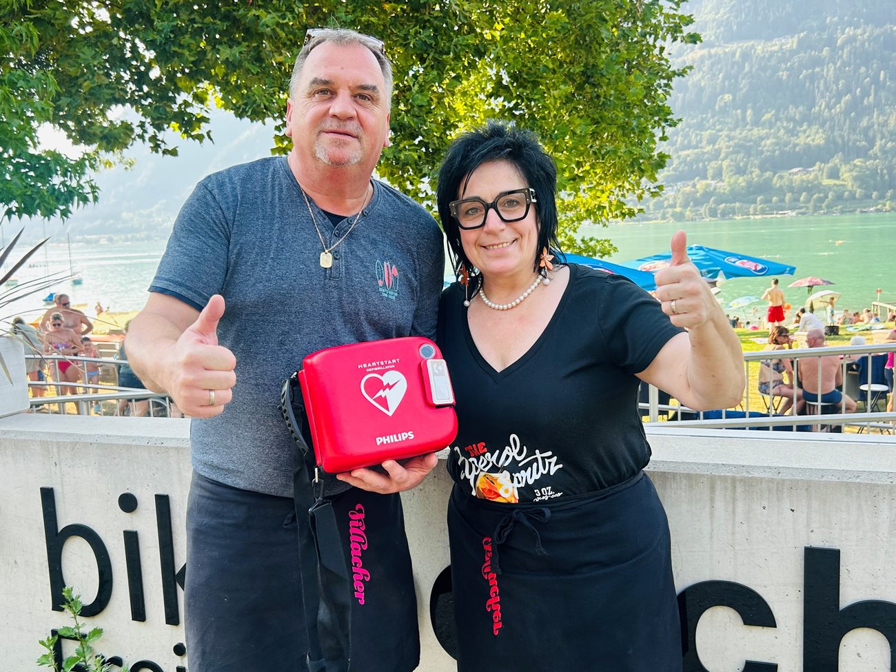 Michaela und und Michael Kopeinig vom Strandbuffet mit dem Defibrillator, der sich zur freien Entnahme im Bereich der Sitztische vor dem Bistro befindet.