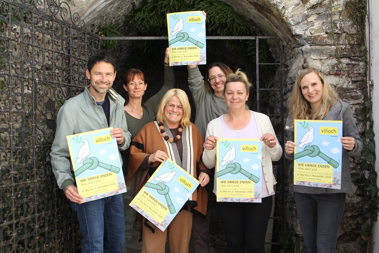 Von Links: Museumsdirektor Andreas Kuchler, Team des Museums und Kulturreferentin Vizebürgermeisterin Gerda Sandriesser stehen vor der Stadtmauer und halten die Plakate zur Sonderausstellung in Händen