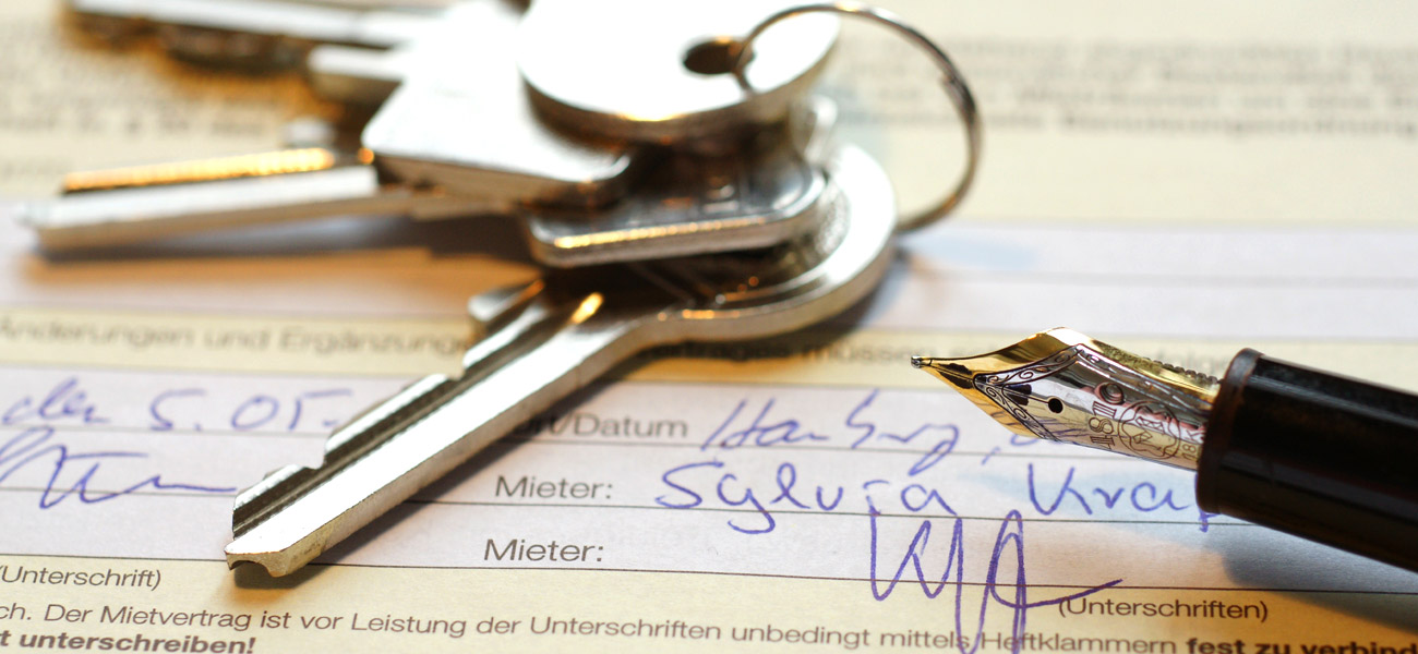 Haustürschlüssel und offene Füllfeder liegen auf unterschriebenen Mietvertrag
