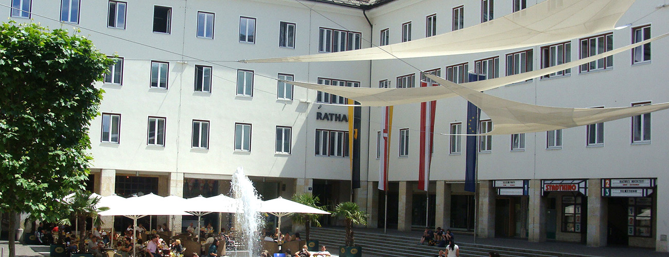 Rathausplatz, Sonnenschirme und Menschen sowie der Springbrunnen