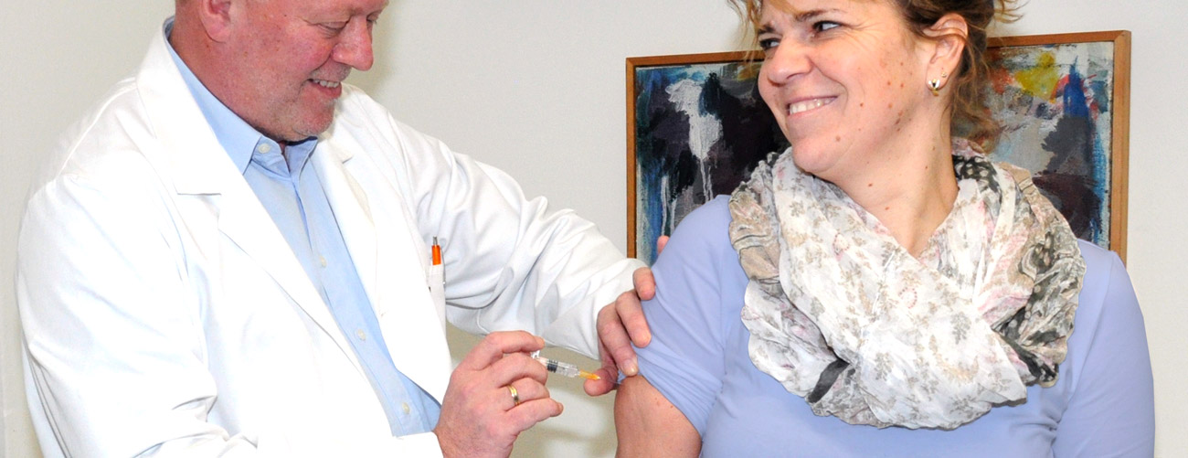Dr. Mack gibt einer Patintinn eine Spritze in den Arm, beide lächeln