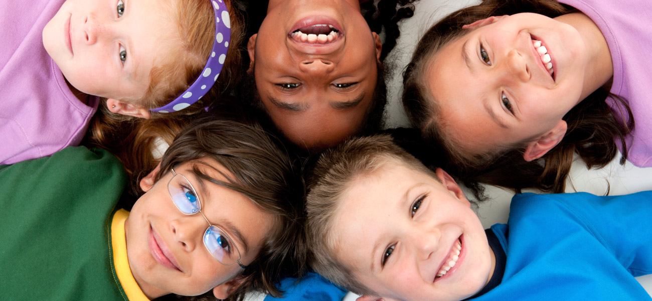Fünf lachende Kinder im Kindergartenalter verschiedenster Nationalitäten liegen im Kreis, Köpfe aneinander