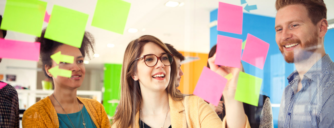 Junge Leute sortieren und beschriften vor einer gläsernen Wand bunte Post-Its