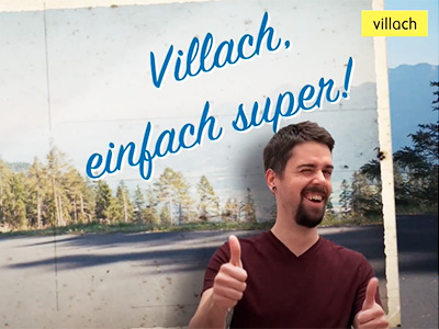 Mann mit Daumen hoch unter einem Plakat mit der Aufschrift "Villach, einfach super!"