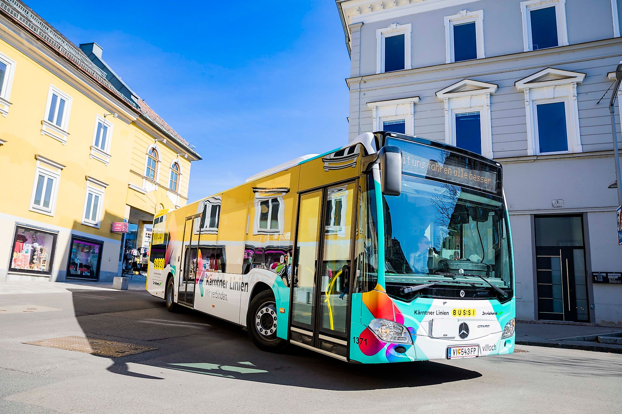 Kärntner Linien Bus in Villach fährt durch eine Gasse mit gelben und grauen Gebäuden.