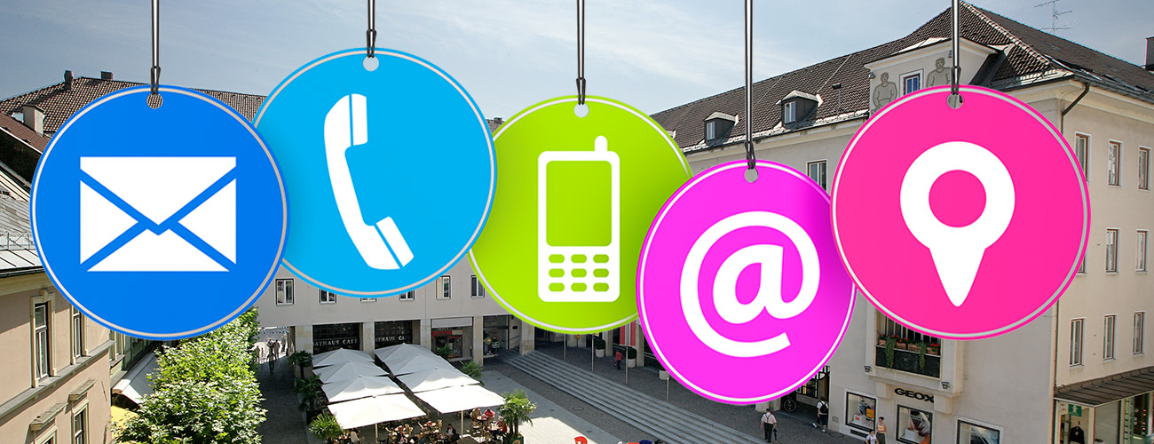 Große, bunte, runde Icons, die die Kontaktmöglichkeiten per E-Mail, Telefon, Handy oder persönlich im Büro signalisieren. Im Hintergrund eine Stadtansicht von Villach.