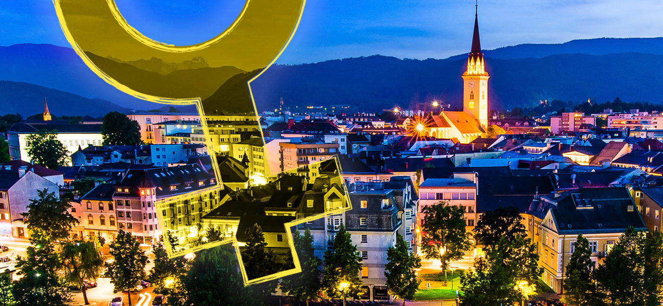 Blick auf die Villacher Altstadt in der Dämmerung, davor groß das Frauen-Zeichen