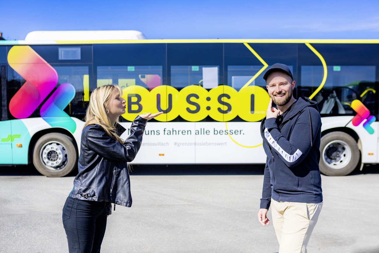 Das Bild zeigt eine Frau, die einem Mann einen Kuss schickt. Im Hintergrund steht ein Bus mit der Aufschrift BUS:SI. 